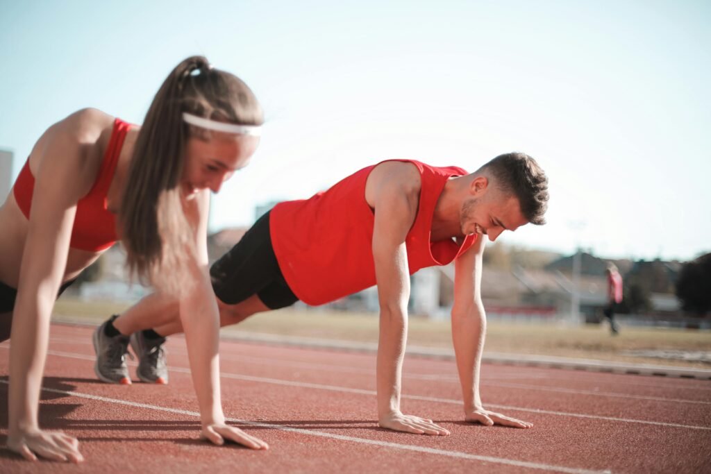 Energetic man and woman performing push-ups on a sunny outdoor track.